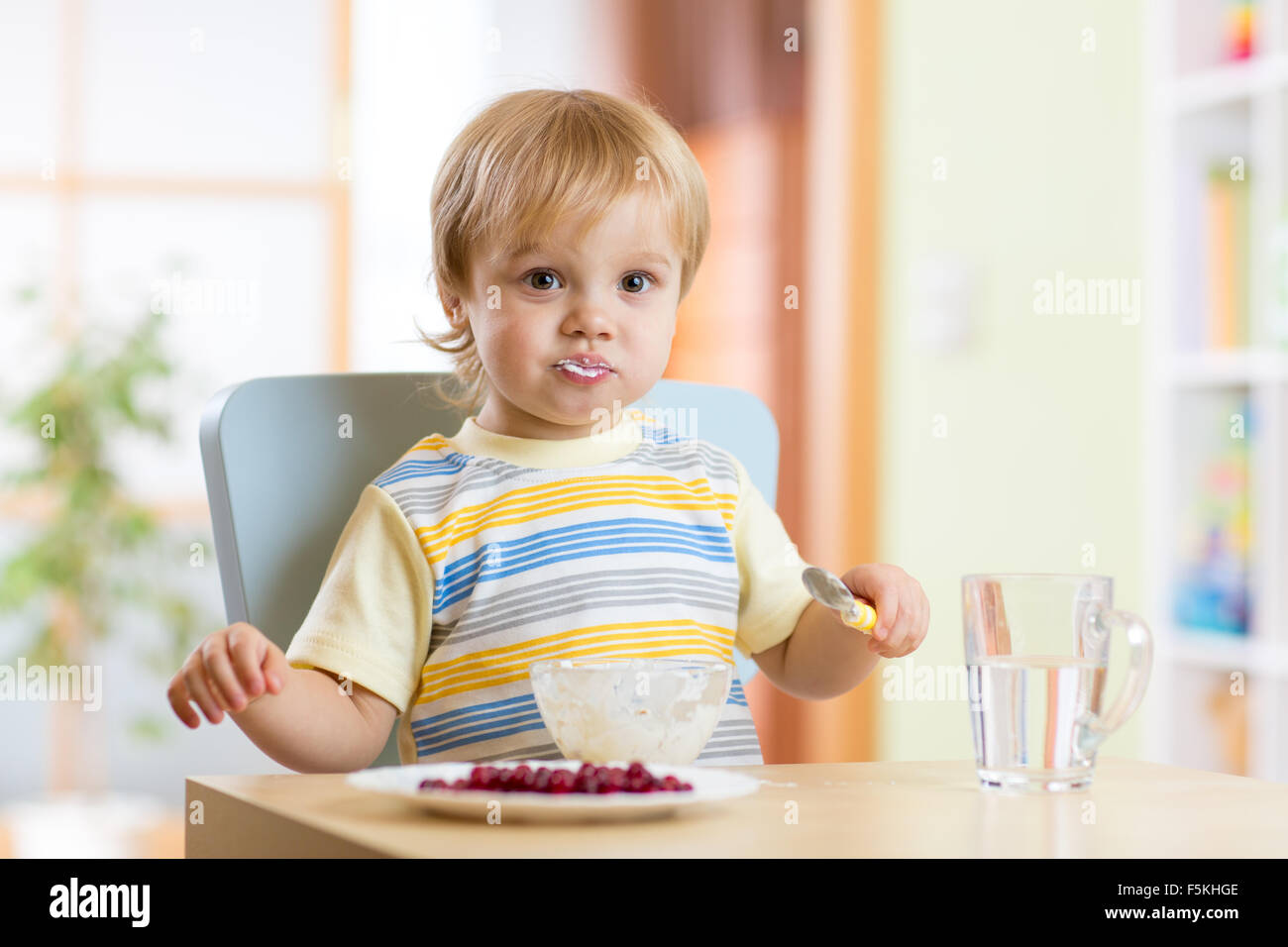Carino bambino piccolo ragazzo mangiare con il cucchiaio nella nursery Foto Stock
