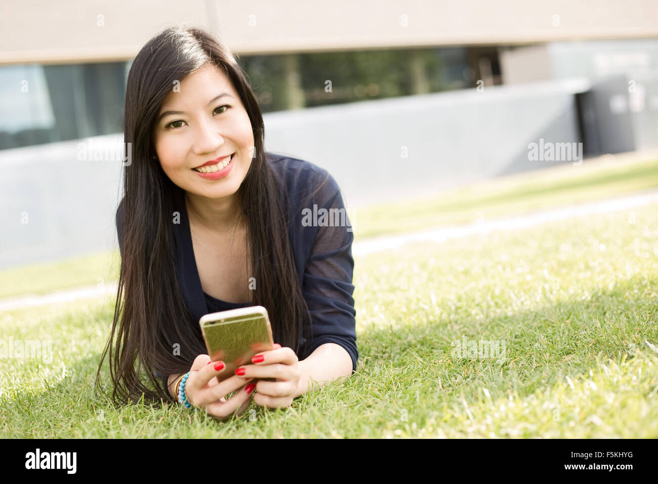Donna giapponese giacente sull'erba tenendo il suo telefono Foto Stock