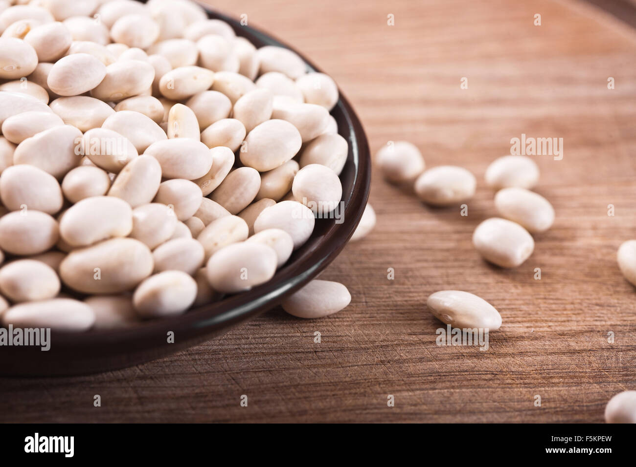 Fagioli bianchi in una piastra marrone su un tavolo di legno, vista dall'alto Foto Stock