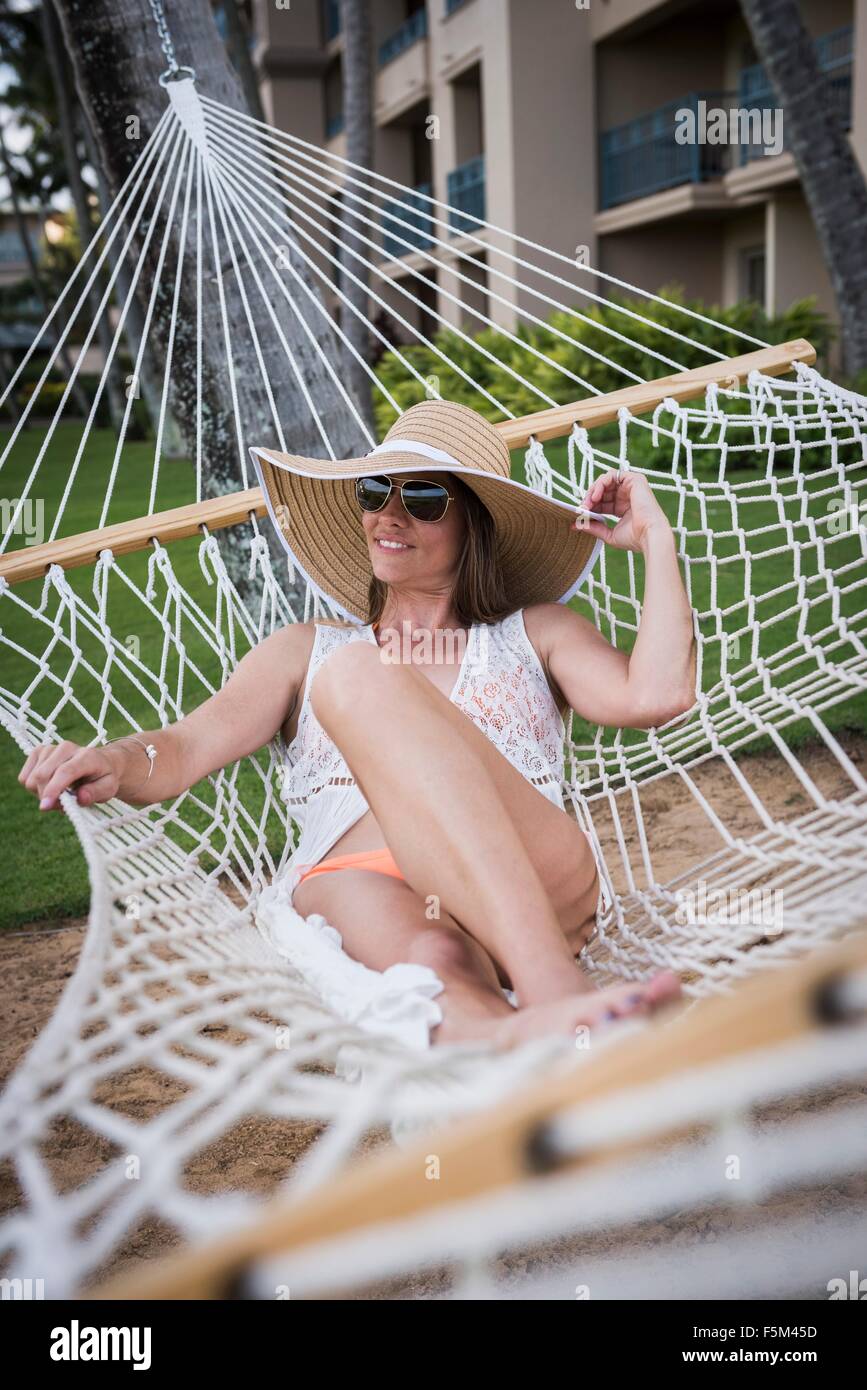 Metà donna adulta indossando cappello e reclinabili bikini in amaca, Maui, Hawaii, STATI UNITI D'AMERICA Foto Stock