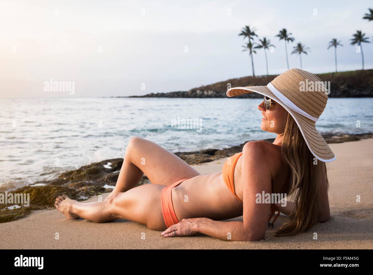 Metà donna adulta indossando cappello e bikini a prendere il sole sulla spiaggia, Maui, Hawaii, STATI UNITI D'AMERICA Foto Stock