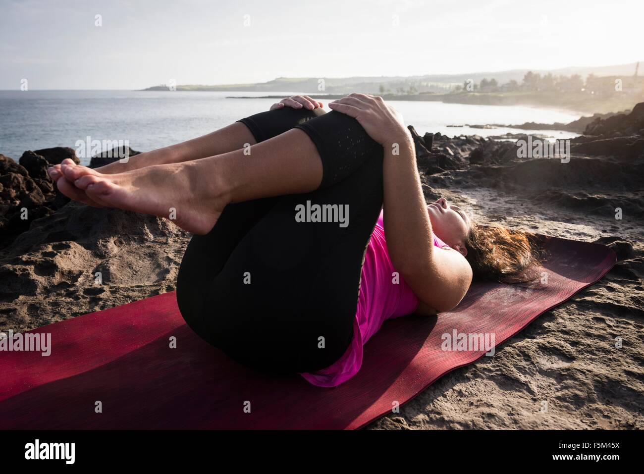 La donna a costa la pratica dello yoga giacente sul retro, punto Hawea, Maui, Hawaii, STATI UNITI D'AMERICA Foto Stock