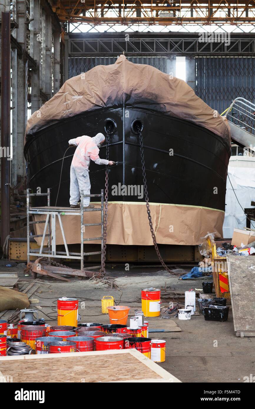 Lavoratore sulla sommità del ponteggio pittura barca in cantiere Foto Stock