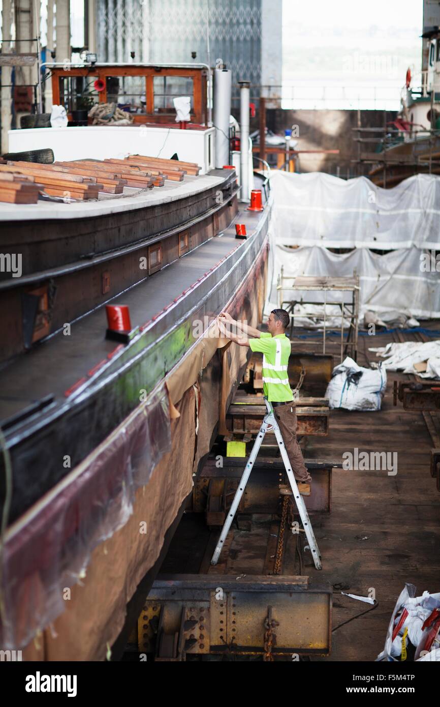 Lavoratore a scaletta controllo barca Cantiere in officina Foto Stock