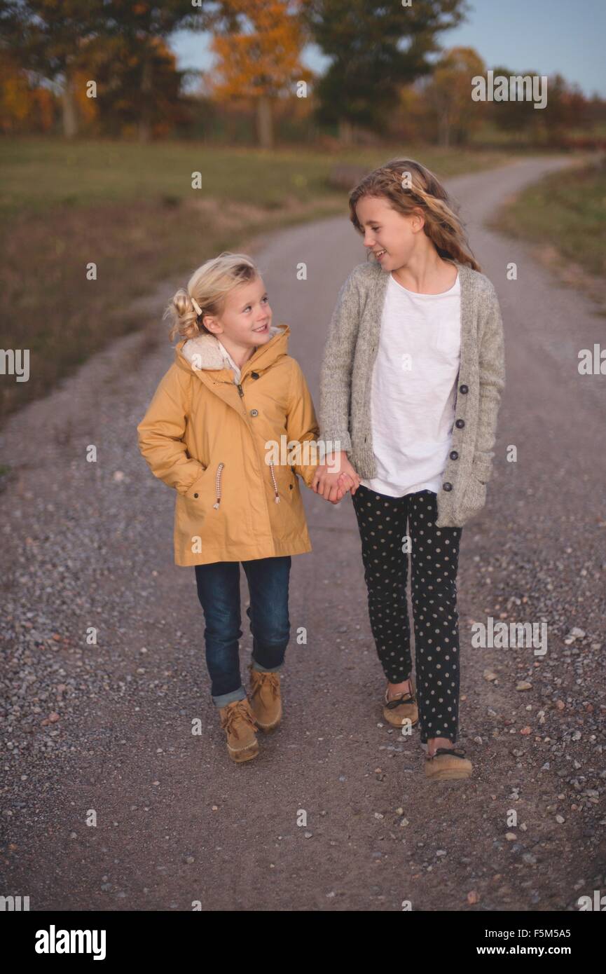 Due giovani ragazze a piedi lungo la strada di campagna, mano nella mano Foto Stock