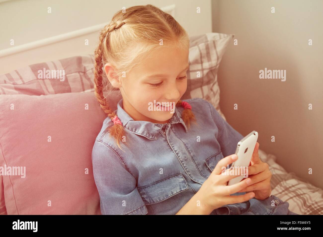 Angolo di Alta Vista della ragazza seduta sul letto che guarda sorridendo dello smartphone Foto Stock