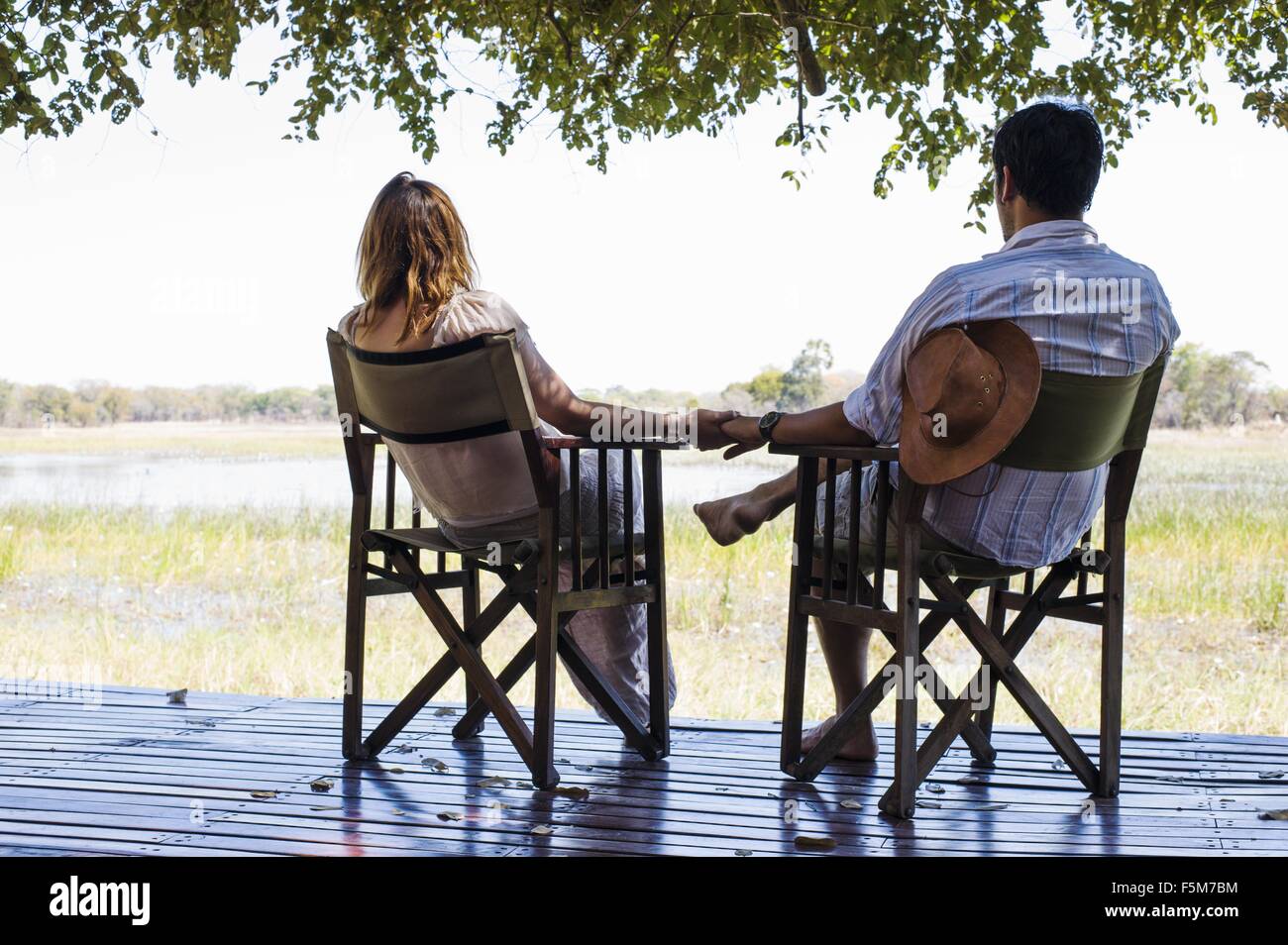 Coppia romantica tenendo le mani mentre seduto al safari lodge, Parco Nazionale di Kafue, Zambia Foto Stock