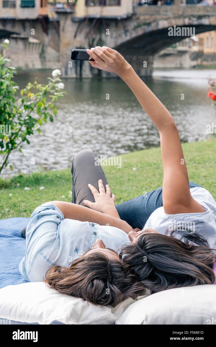 Lesbica giovane sdraiato utilizza lo smartphone per prendere selfie nella parte anteriore del Ponte Vecchio oltre il fiume Arno, Firenze, Toscana, Italia Foto Stock