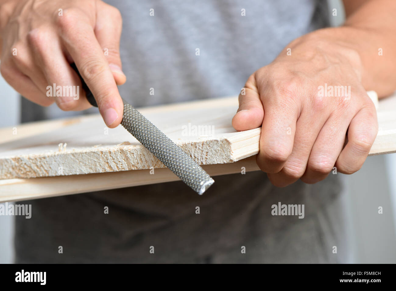 Primo piano di un giovane uomo caucasico il deposito di un pannello di legno con una raspa Foto Stock