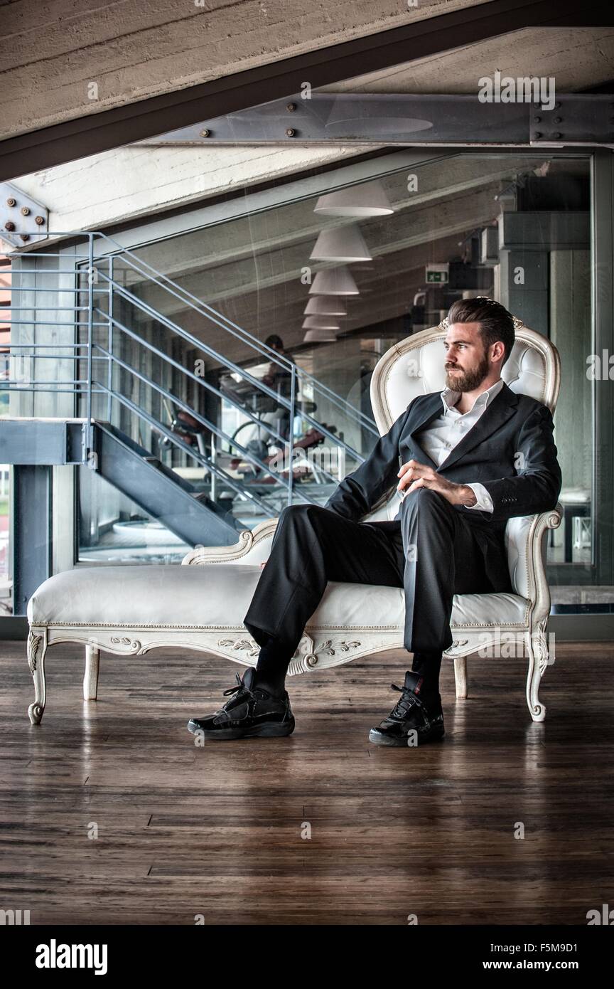 Metà uomo adulto indossare tuta seduto sulla chaise lounge che guarda lontano Foto Stock
