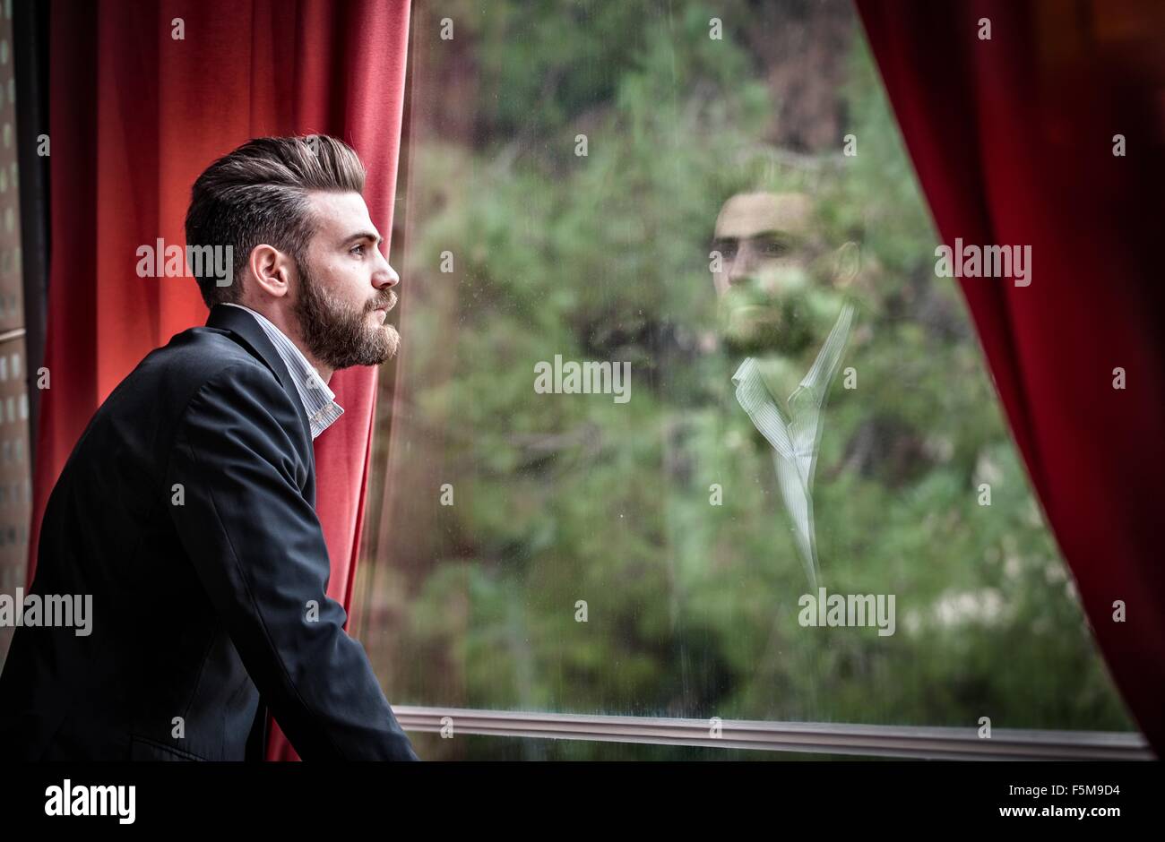 Vista laterale della metà uomo adulto indossare tuta guardando fuori della finestra Foto Stock