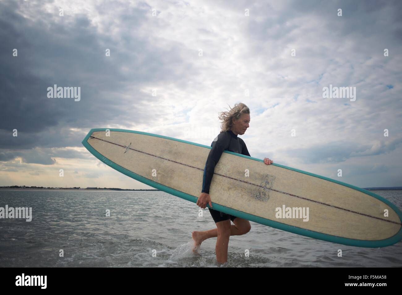 Senior donna a piedi dal mare, portando le tavole da surf Foto Stock