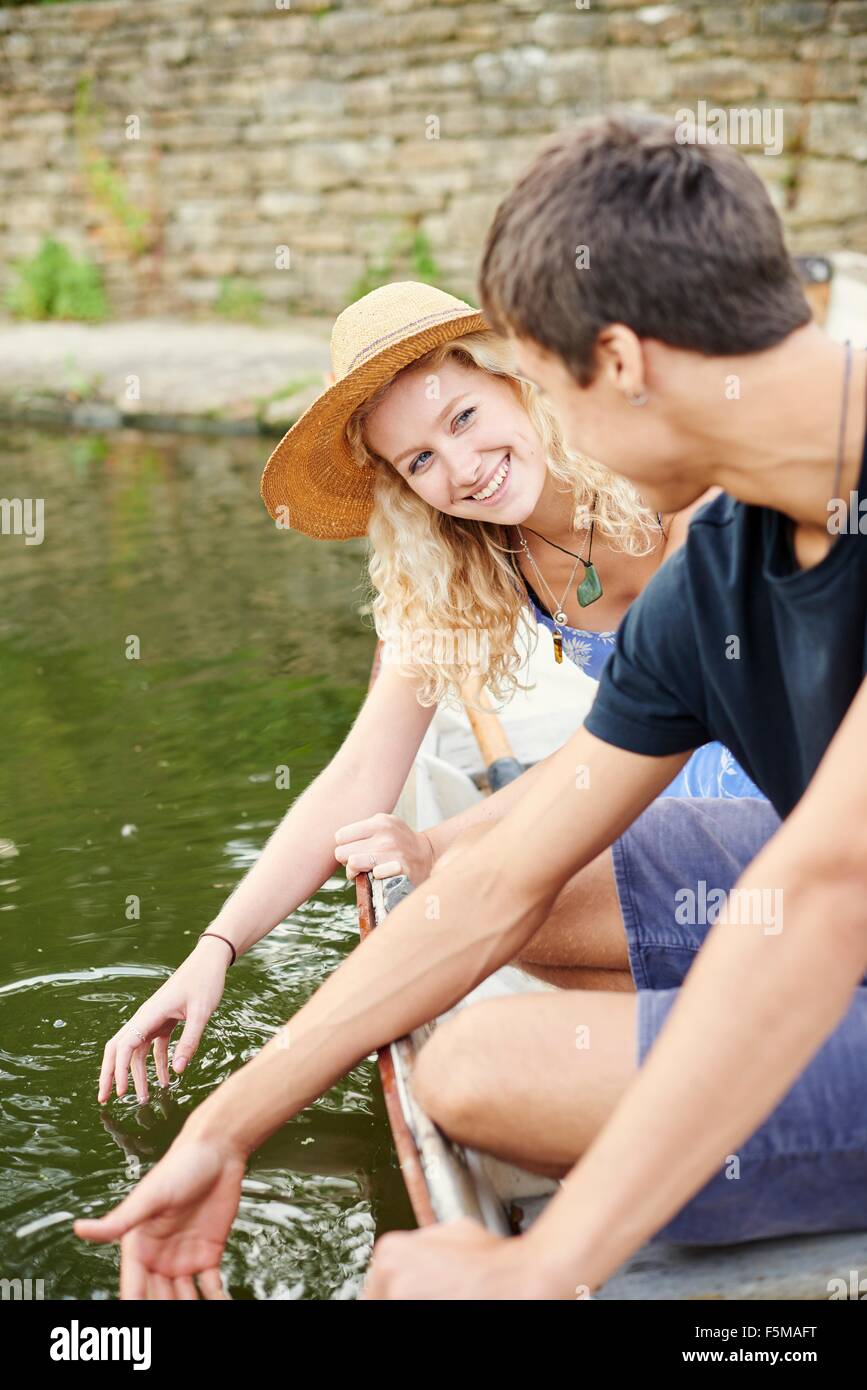 Coppia giovane toccando acqua dalla barca a remi sul fiume rurale Foto Stock
