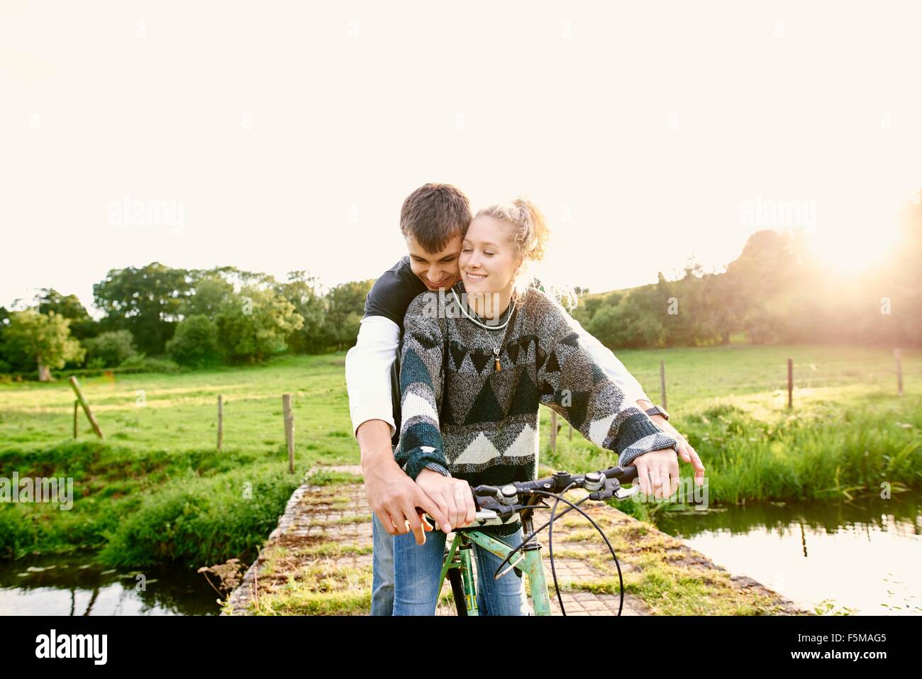 Coppia giovane la condivisione bicicletta alla passerella sul fiume Foto Stock