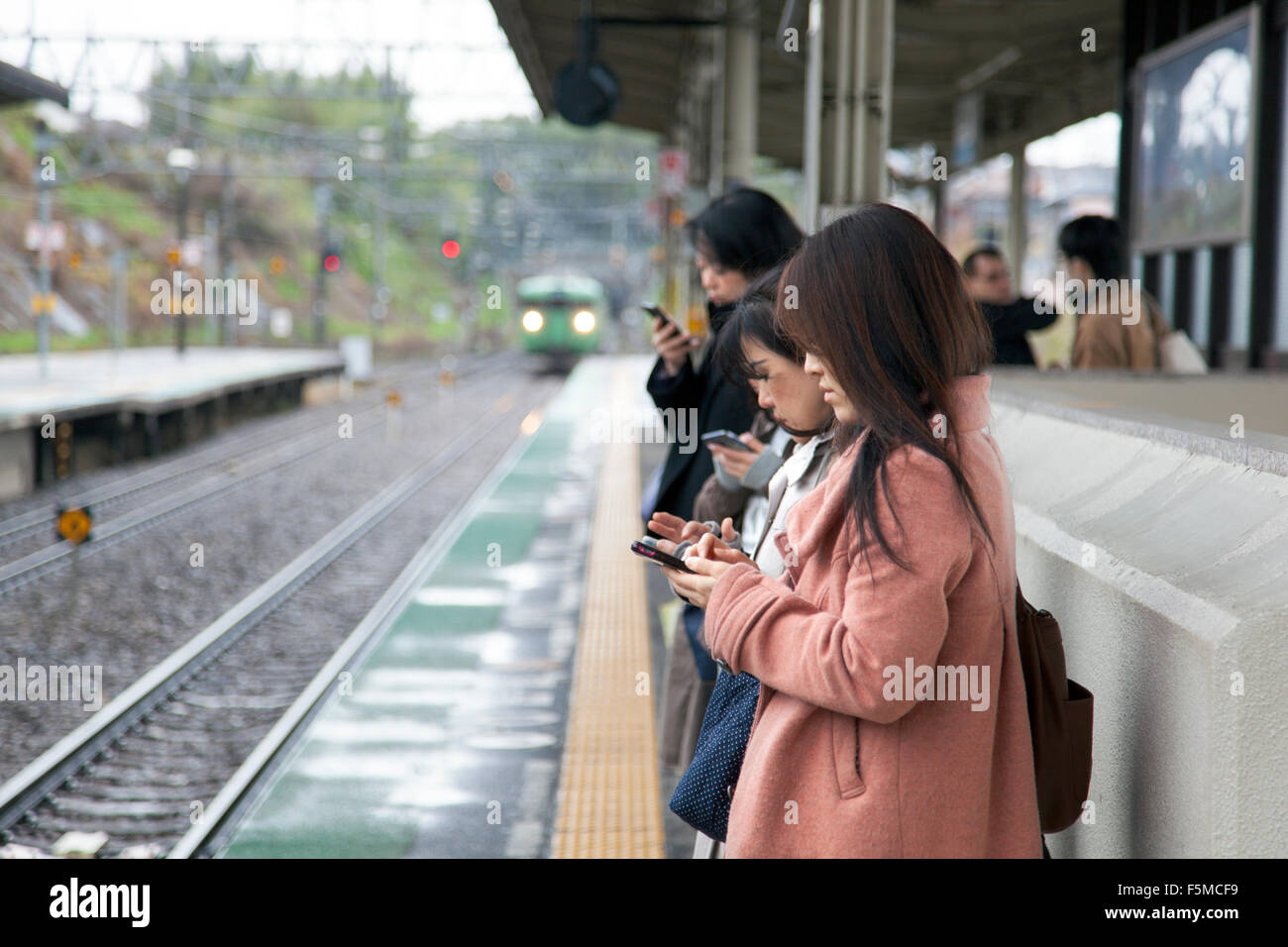 Ragazze utilizzando i telefoni cellulari in attesa di un treno, Giappone Foto Stock