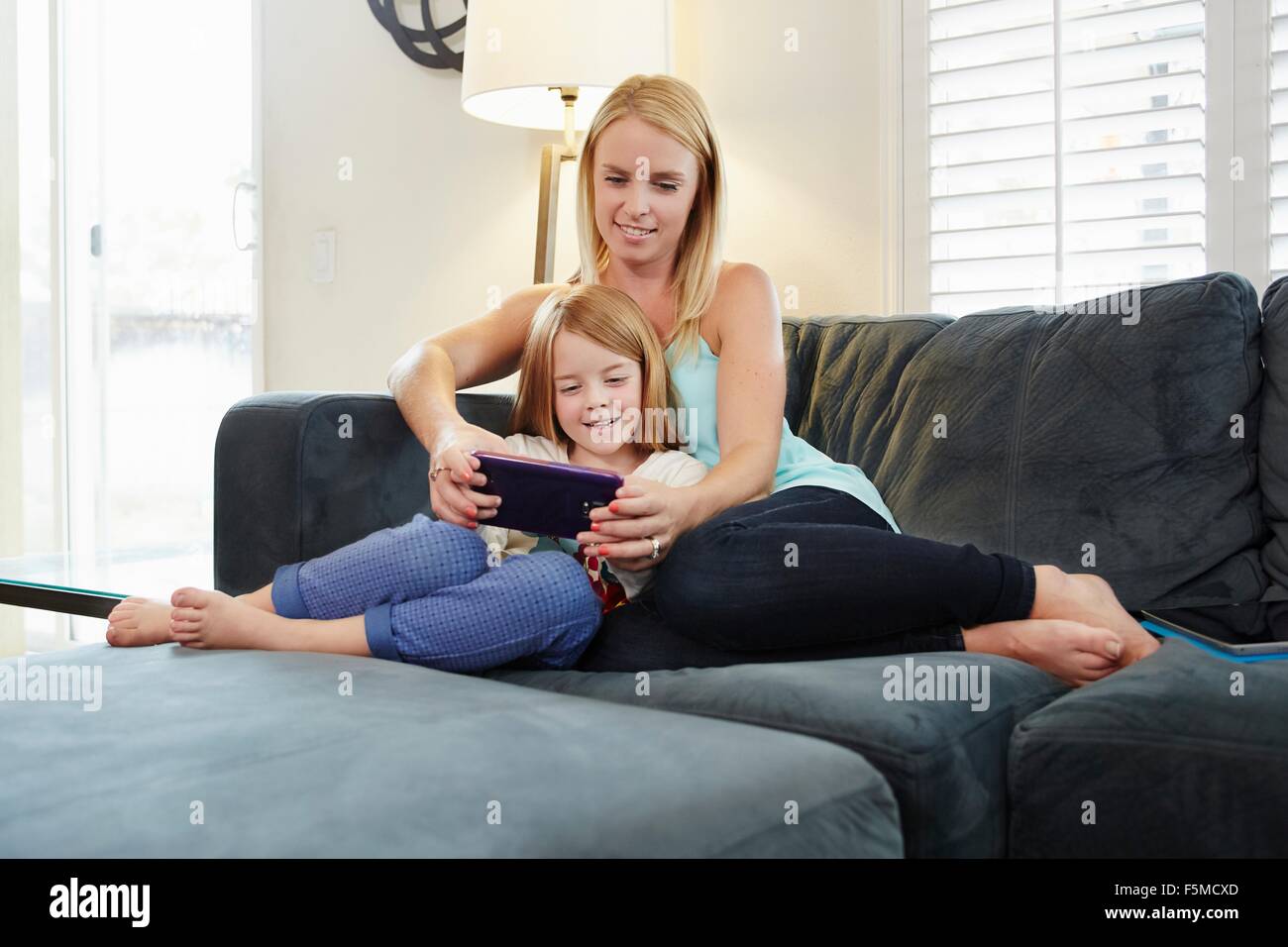 Madre e figlia con tavoletta digitale sul divano nel soggiorno Foto Stock