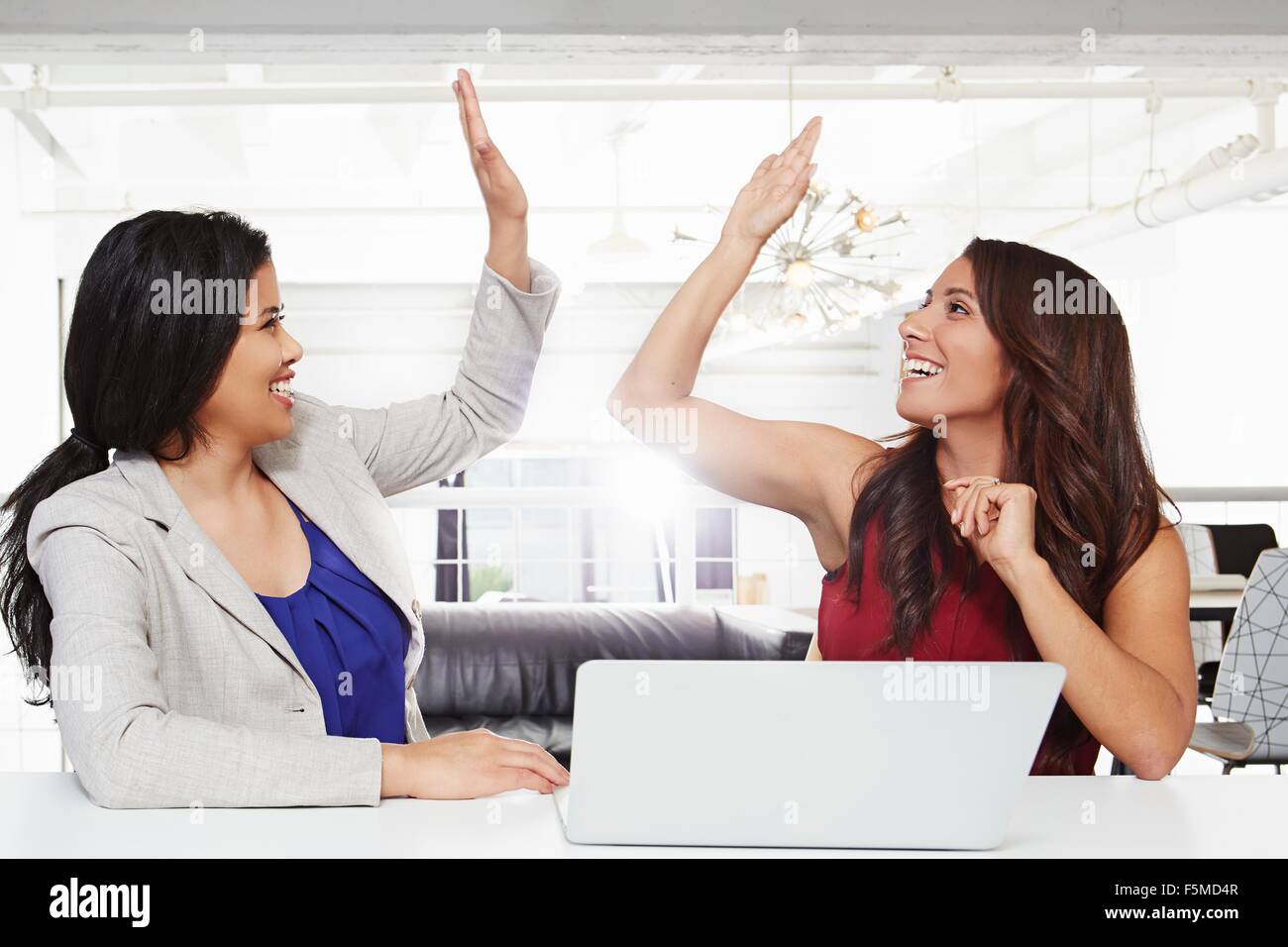 Due imprenditrici seduto alla scrivania, dando alta cinque Foto Stock