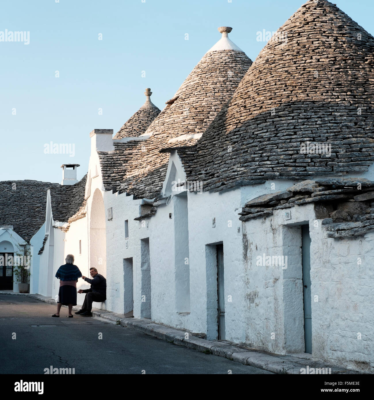 Un uomo anziano e donne chat fuori i Trulli di Alberobello, provincia di bari, puglia, Italia Foto Stock