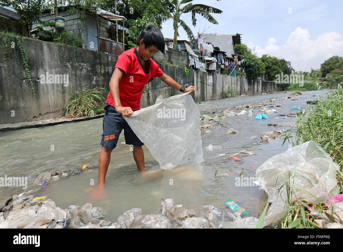 Un ragazzo lava i fogli di plastica in un flusso per fornirli al riciclaggio. In prossimità di una discarica di rifiuti in Montablan, Quezon City, Manila, Filippine Foto Stock