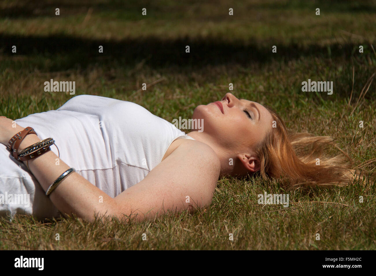 Un attraente giovane donna giaceva a terra addormentato sotto un albero con gli occhi chiusi. Foto Stock