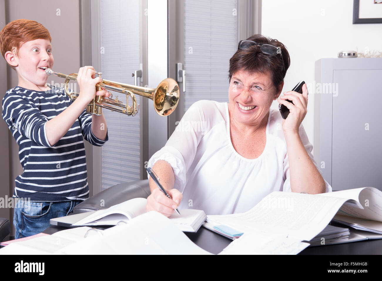 La madre lavora in un home office, figlio è inquietante da suonare la tromba Foto Stock