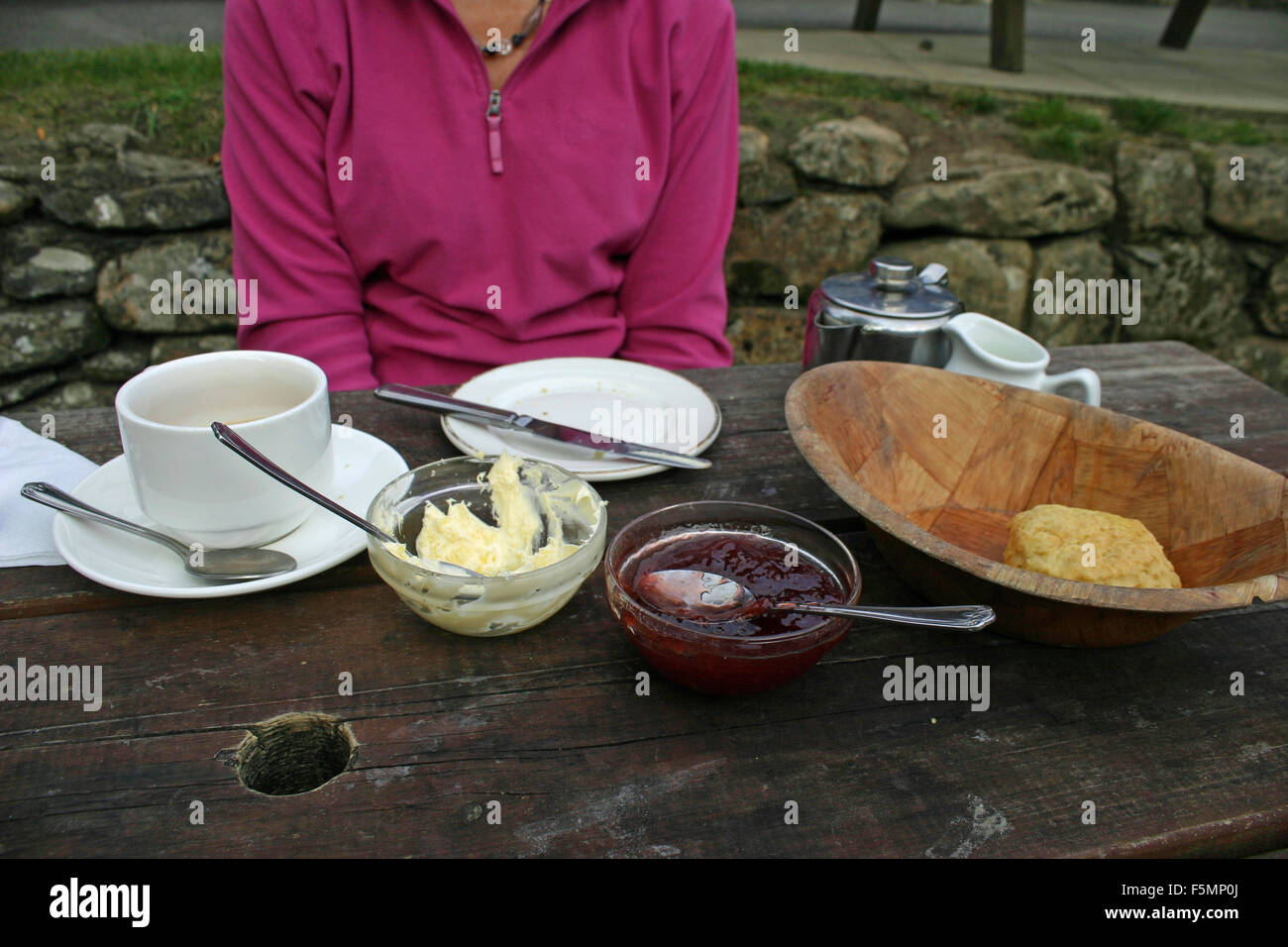 Persona non identificabili seduto al banco di picnic dopo aver mangiato un tè alla crema in un pub giardino. Tè, cornetto, crema e marmellata sul tavolo con stoviglie e posate. Foto Stock