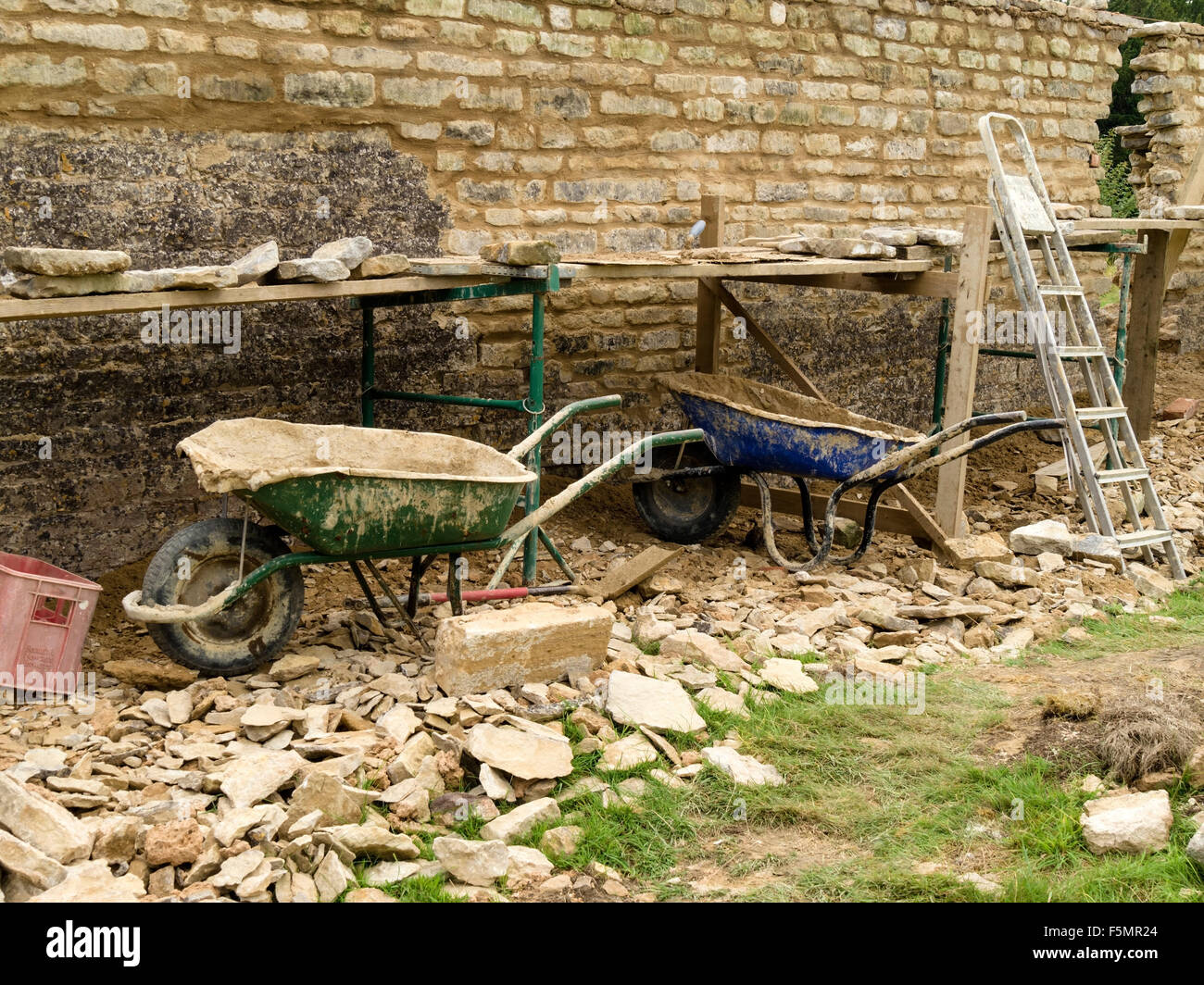 Vecchio naturale, giardino di pietra calcarea parete riparazioni e ristrutturazioni con builder strumenti, carriole, tralicci, ponteggi e tavole. Foto Stock