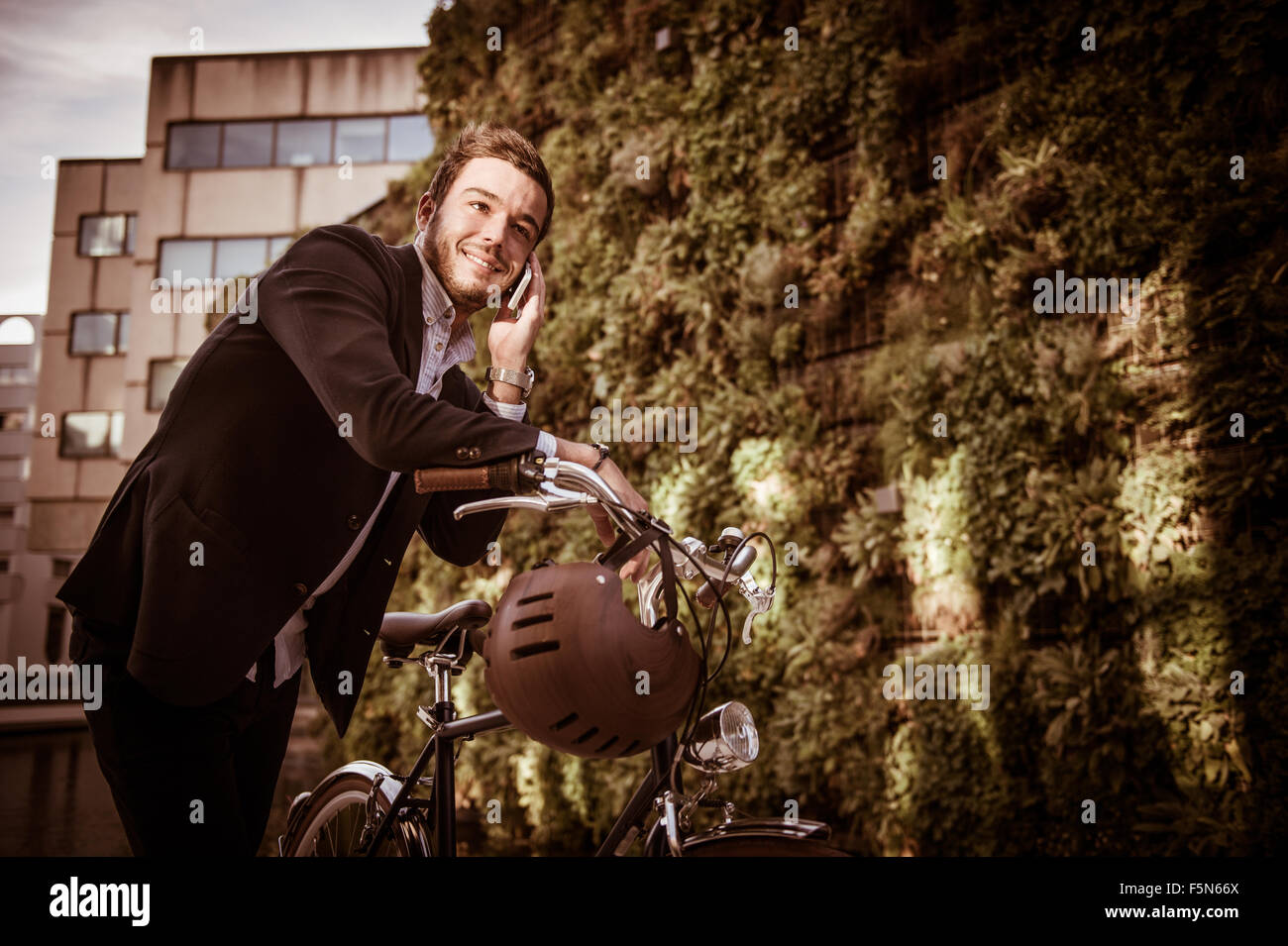 Imprenditore parlando al cellulare seduti sulla sua bicicletta in città Foto Stock
