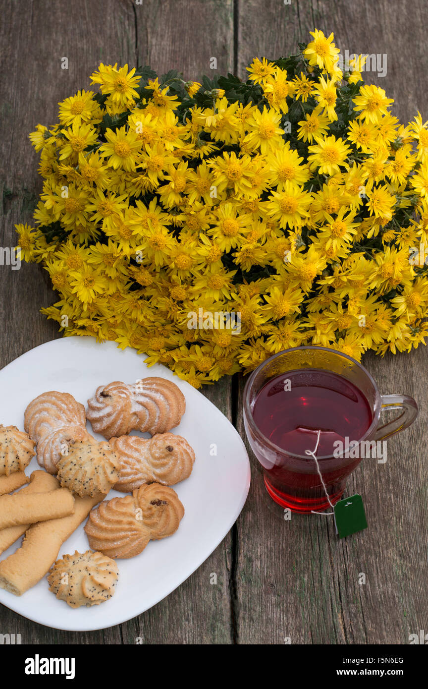 Bicchiere di tè, bouquet di fiori di colore giallo e la piastra con i cookie Foto Stock