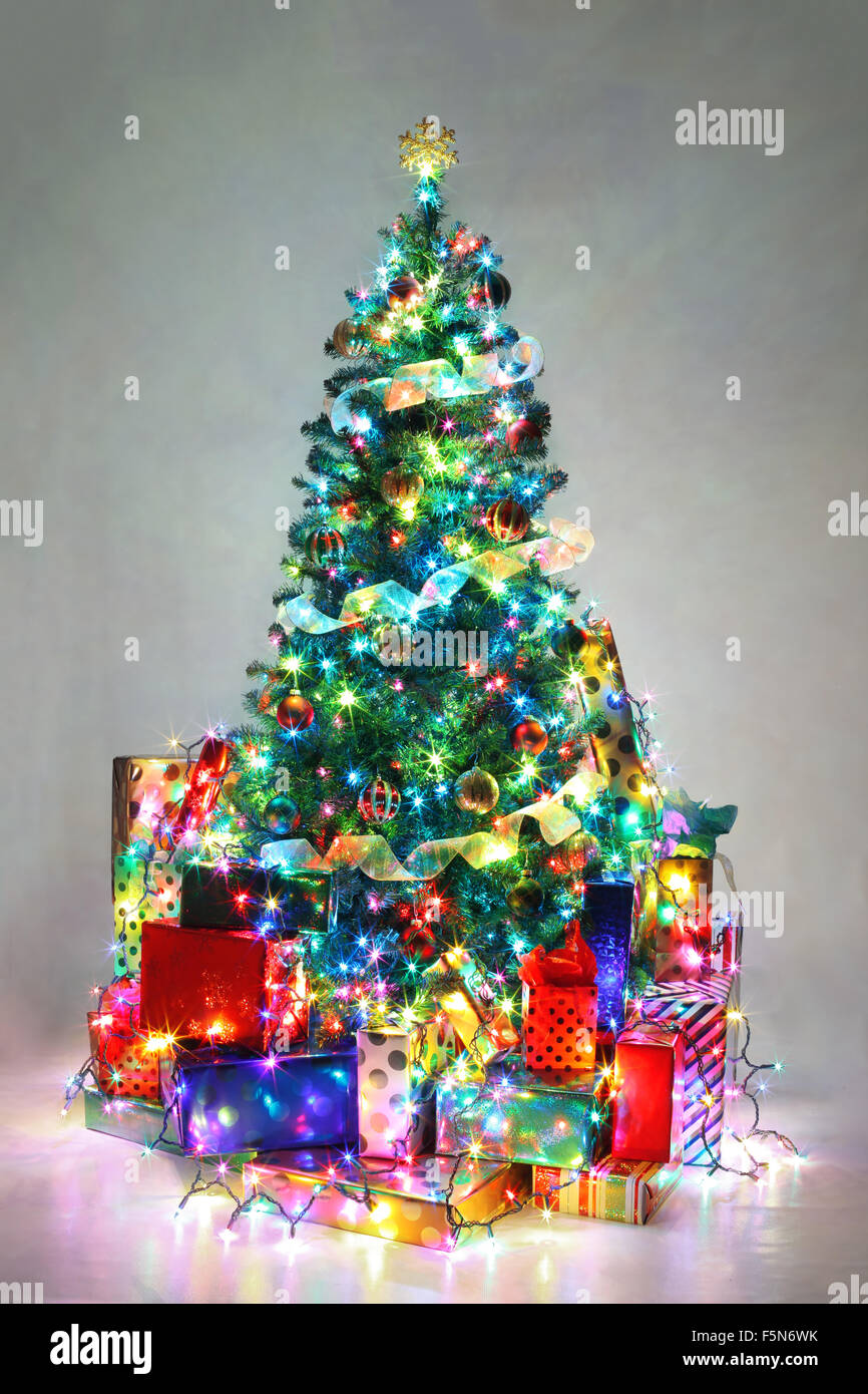 Albero di Natale decorato con luci colorate circondato da presenta. Foto Stock