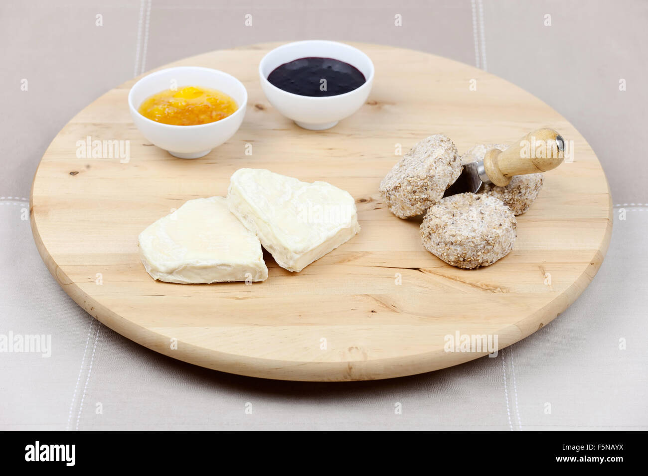 Formaggio di capra a forma di cuore e ricoperta con semi di sesamo con, Coltello per formaggio, aspro marmellata di arance e confettura di more sul round woo Foto Stock