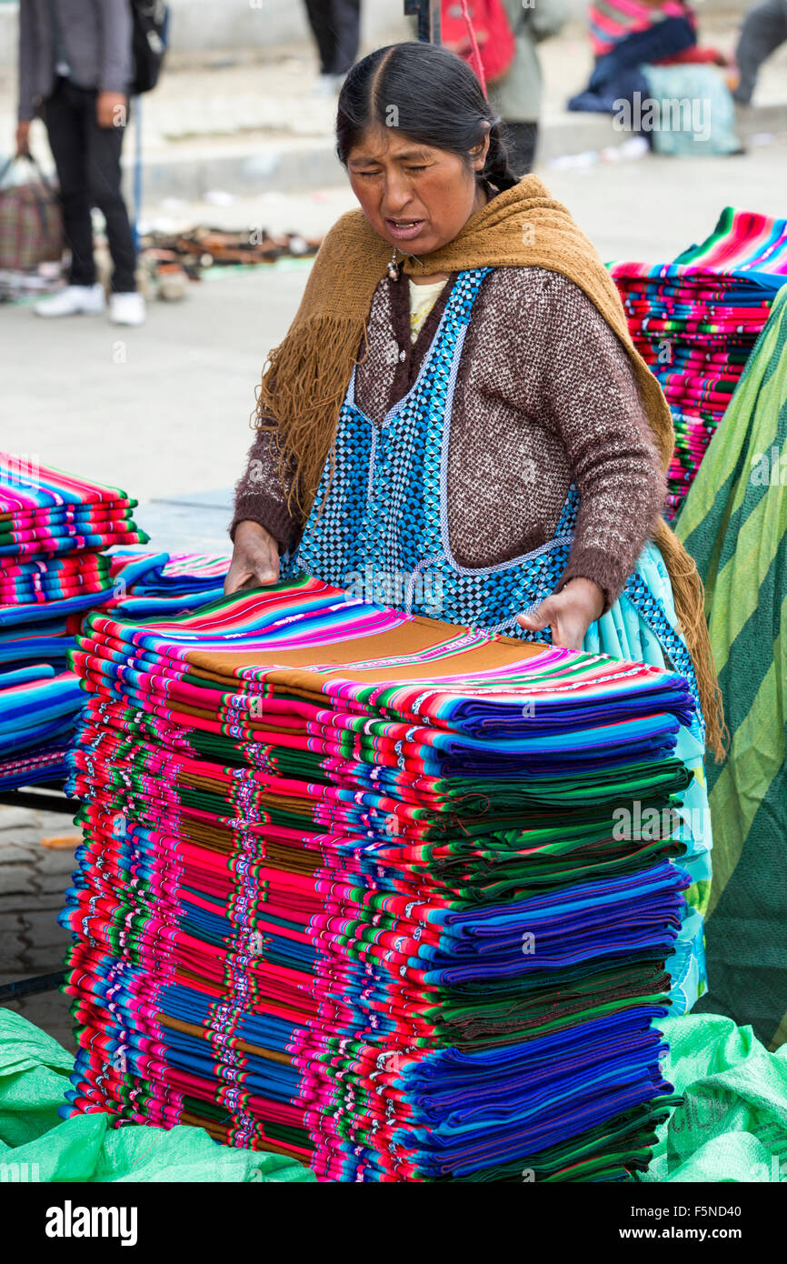 Una donna indigena tradizionale di vendita colorato tessuto boliviano ad una strada del mercato di El Alto, La Paz, Bolivia, Sud America. Foto Stock