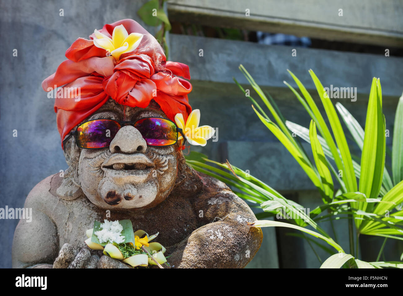 Divertente volto ritratto di vecchio stile Balinese tradizionale tempio statua di guardia vestiti in divertenti costume turistica con occhiali da sole. Foto Stock