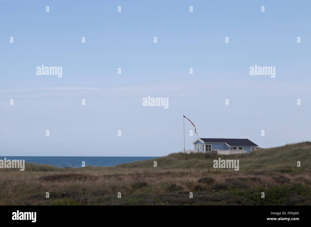 Una casa estiva di tutto da solo si erge proprio sul bordo di una scogliera che si affaccia sul Mare del Nord orgogliosamente battenti un gagliardetto bandiera danese. Foto Stock