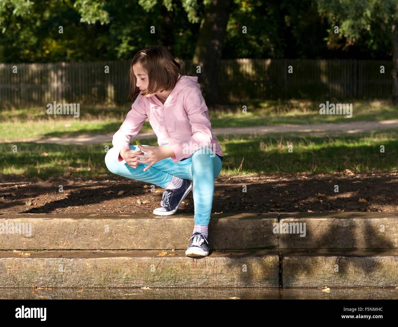Una giovane ragazza squat molto elegantemente accanto a un flusso assente mindedly giocando con una foglia mentre è nel profondo del pensiero. Foto Stock