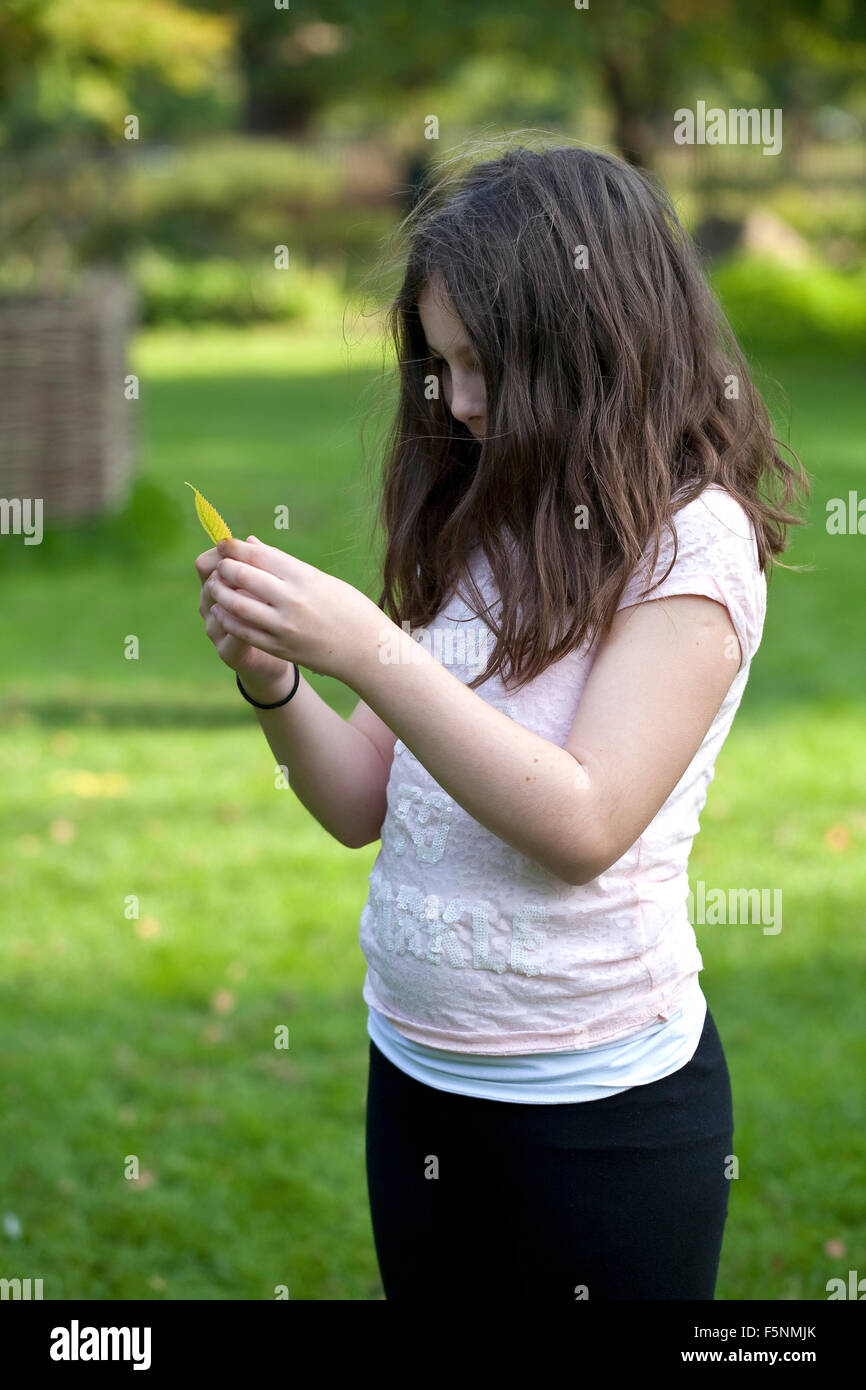 Un giovane dai capelli scuri ragazza sta guardando intensamente a una foglia d'autunno. Foto Stock