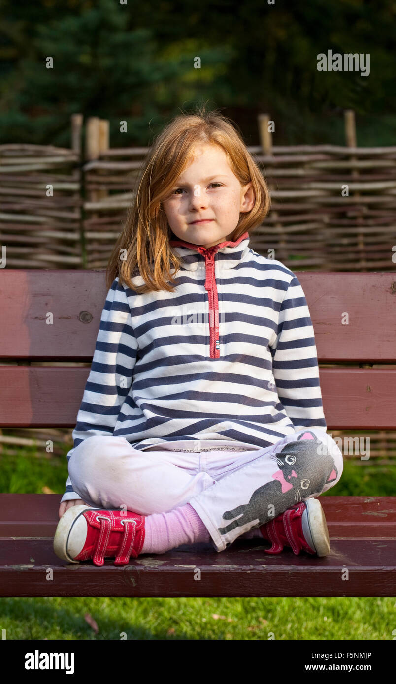 Una giovane ragazza è seduta zampe trasversale su un banco di lavoro. Lei sta cercando a destra alla fotocamera Foto Stock