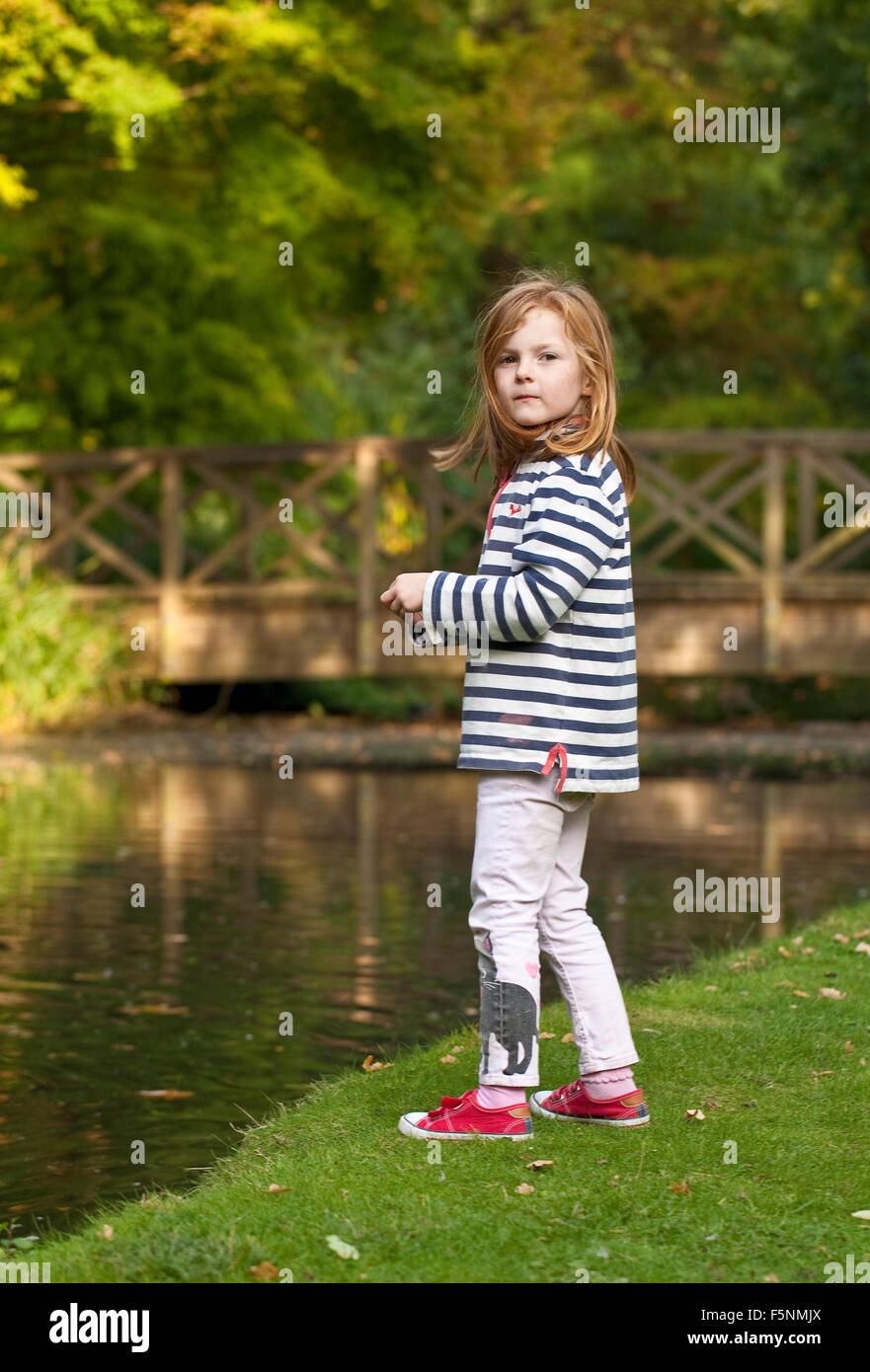 Una giovane ragazza è fuori ad esplorare un parco con un laghetto. Foto Stock