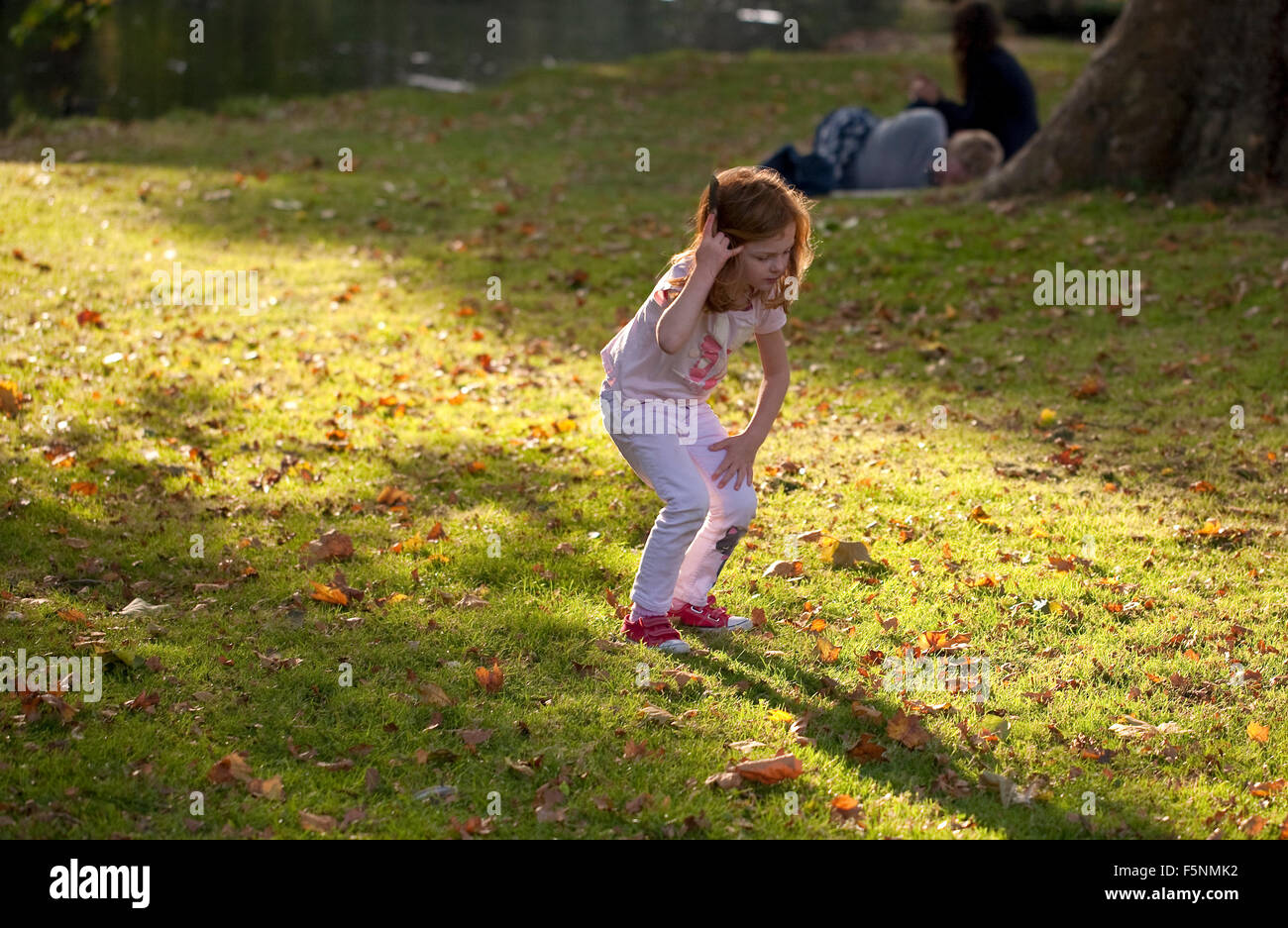Una giovane ragazza cerca attraverso le foglie cercando conkers caduti. Essa si erge in un flusso di luce del sole che trattiene i suoi capelli. Foto Stock