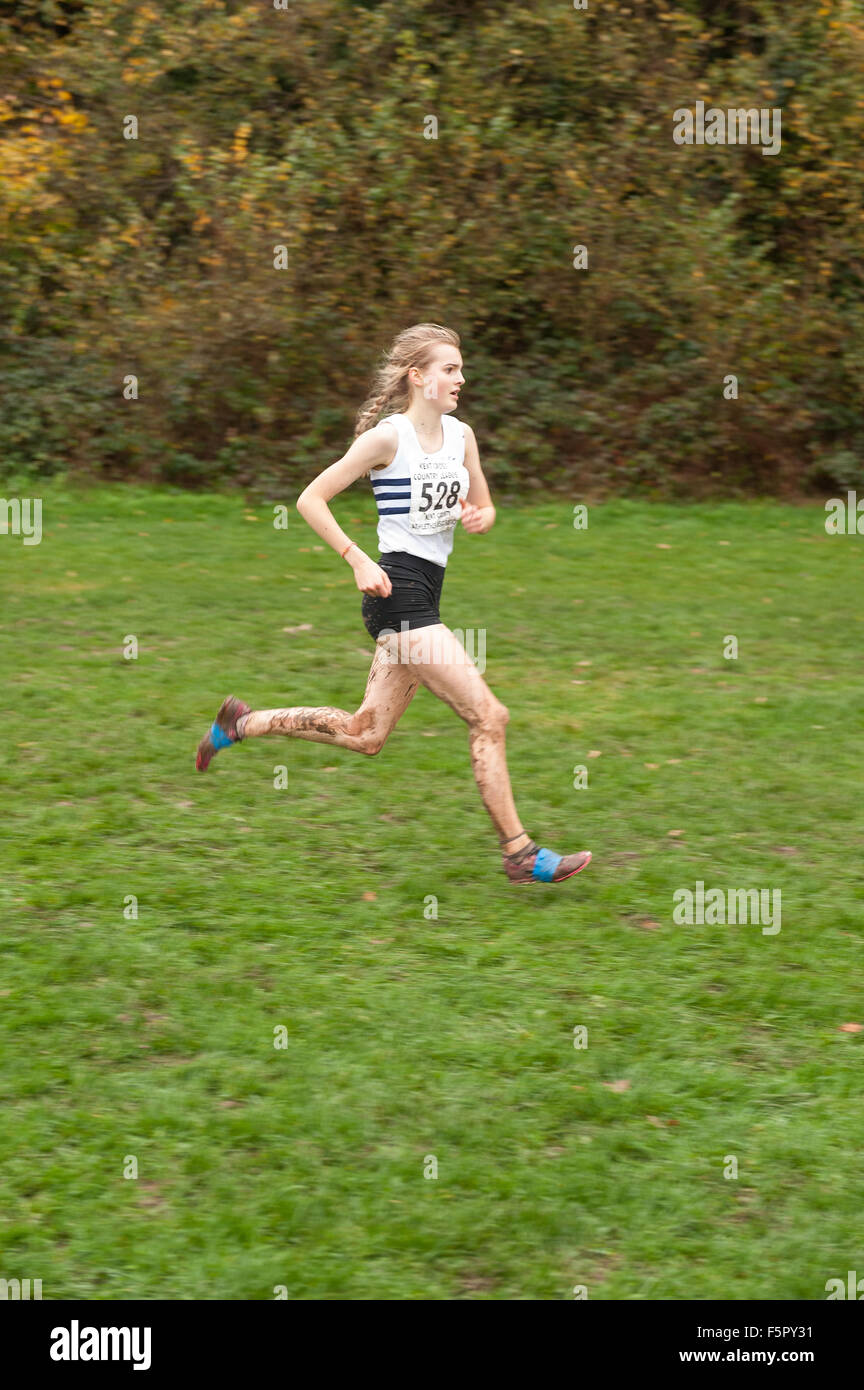 La bionda signora giovane runner rivestito in pioggia e fango affacciate agli elementi nel cross country race con silenziatore campo di erba al calpestio Foto Stock