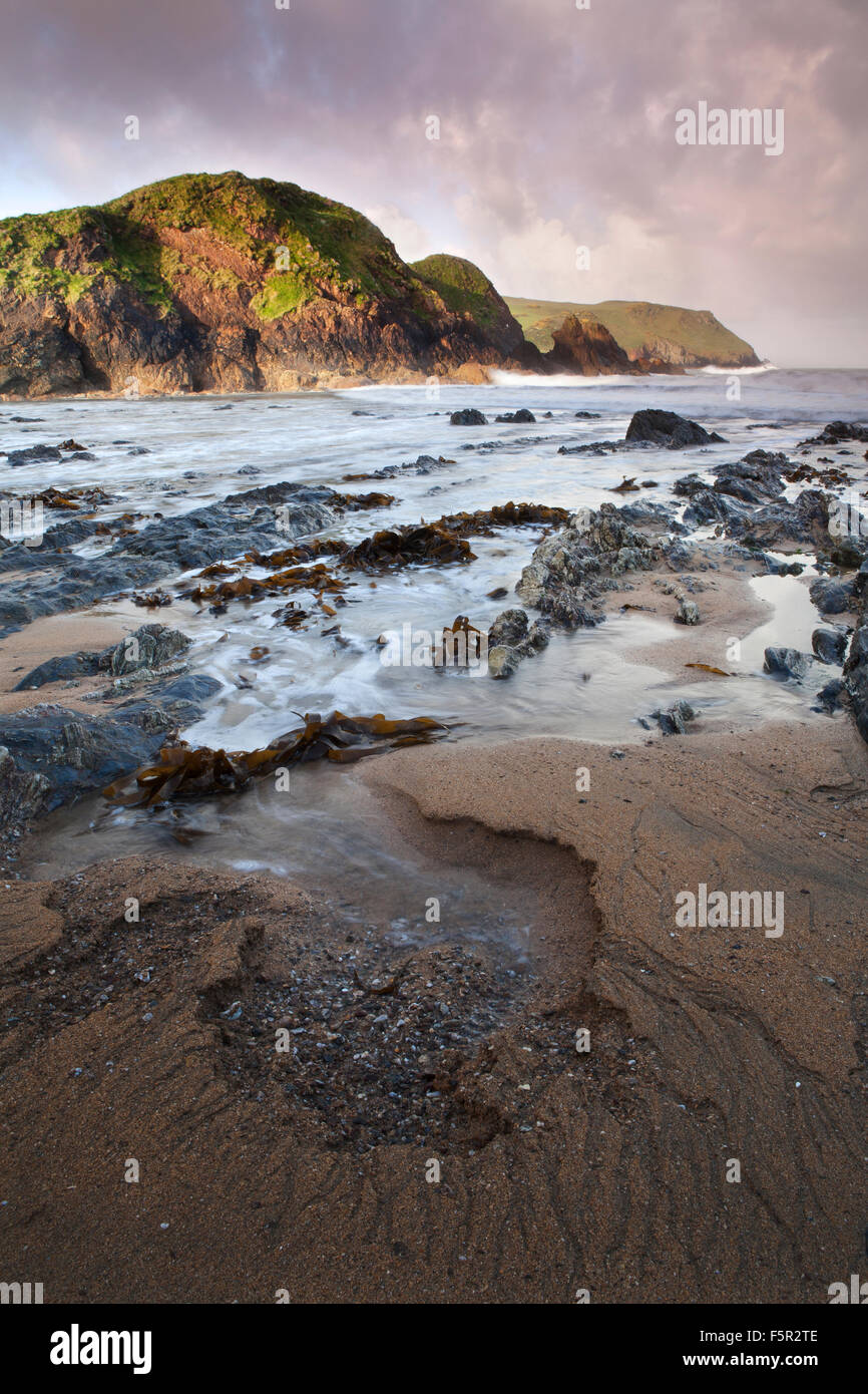 I motivi sono lasciati nella sabbia dalla marea azione e come le onde si inclinano e frastagliate rocce e alghe sono lasciati sulla spiaggia Mouthwell. Foto Stock