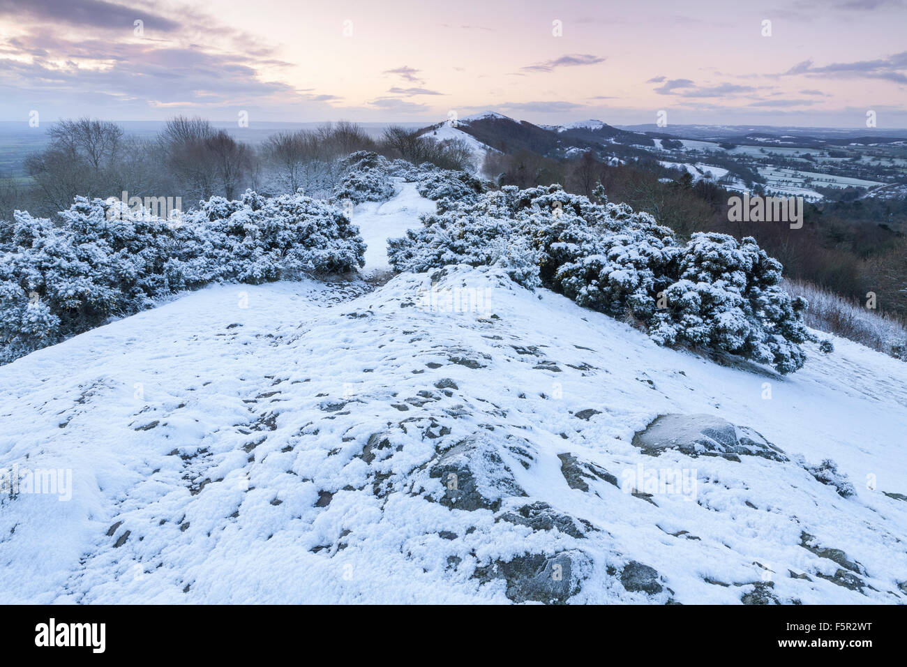 Una debole sunrise è colata luce morbida sulla neve percorso coperto di estate Hill, Malvern Hills, Worcestershire Foto Stock