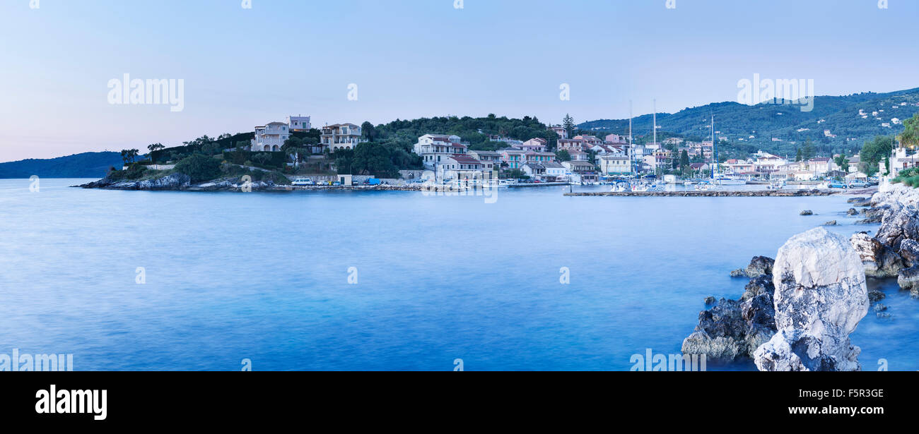 Kassiopi nella luce del mattino. Un cast blu copre l'acqua e cielo con occasionali bagliore arancione dalle luci della strada. Foto Stock