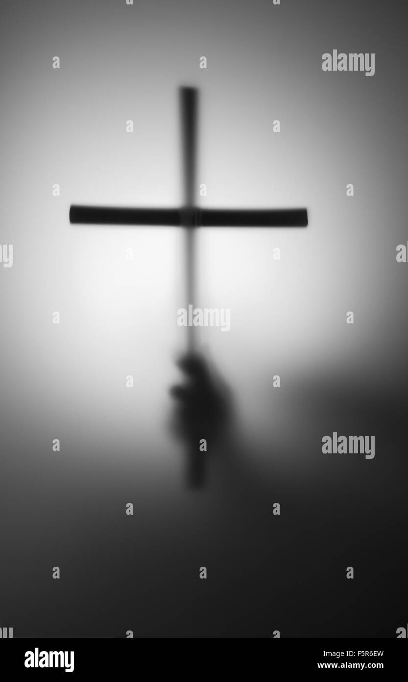 Silhouette offuscata della mano con la croce nel buio Foto Stock