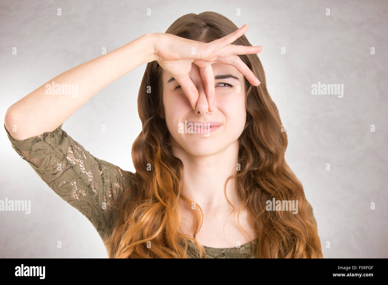 Copertura femmina il suo naso con una mano, isolato in uno sfondo grigio Foto Stock