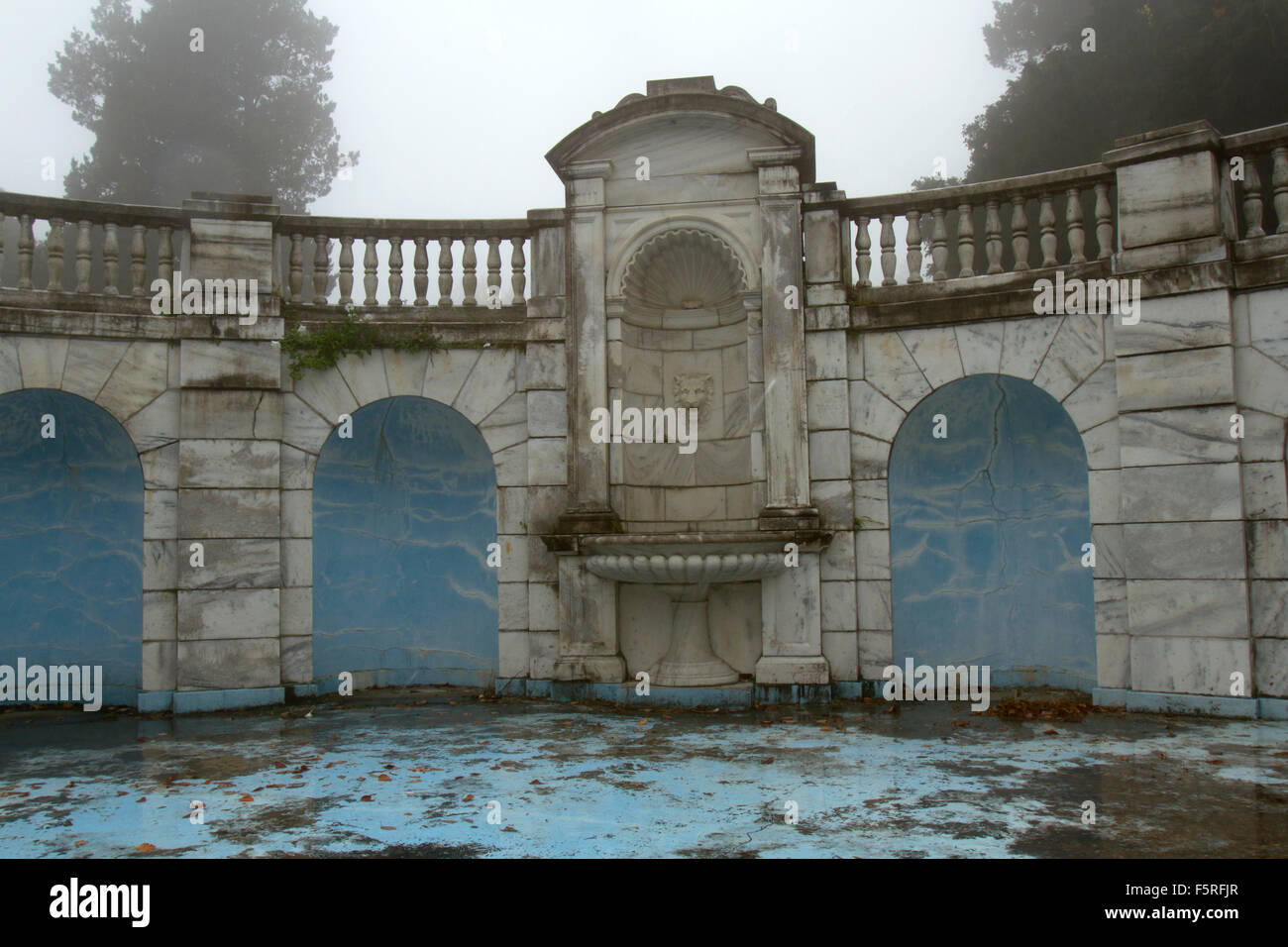 Fontana in marmo in disrepairs nel giardino formale di pioggia, nebbioso giorno. Foto Stock