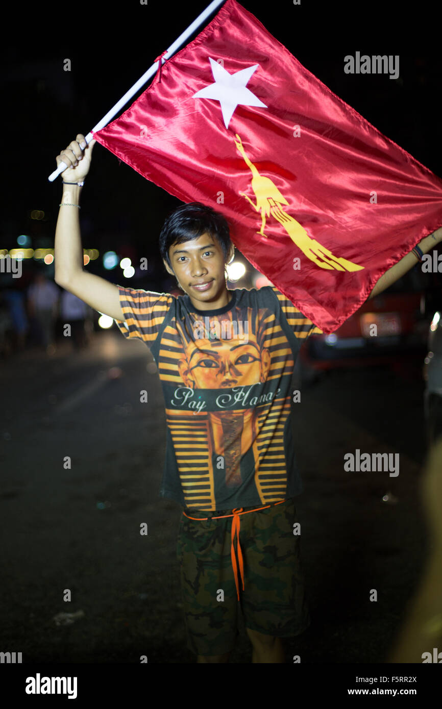 Yangon, Myanmar, 8 Novembre 2015: come la folla si disperdono dopo la raccolta al di fuori della NLD uffici, un ragazzo pone con una bandiera della NLD Foto Stock