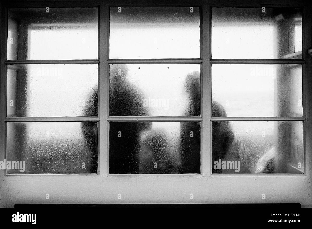 Una famiglia riparo dalla pioggia in un rifugio sul lungomare, fotografata attraverso il bagnato in vetro smerigliato. Foto Stock