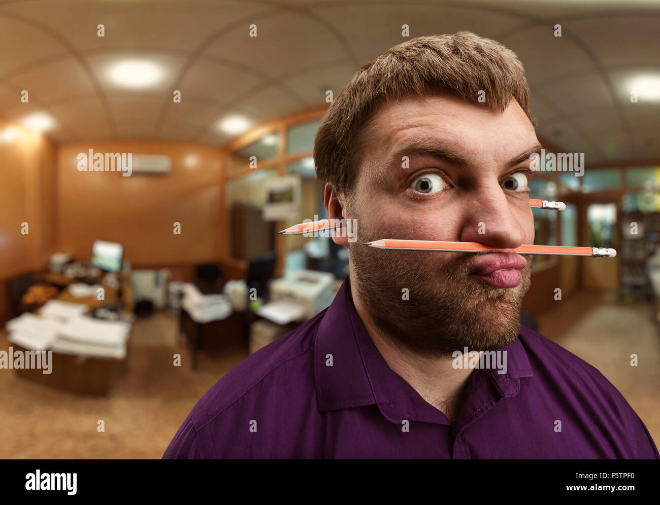 Strano uomo barbuto detiene una matita con il suo naso e le labbra e più una matita nelle orecchie Foto Stock