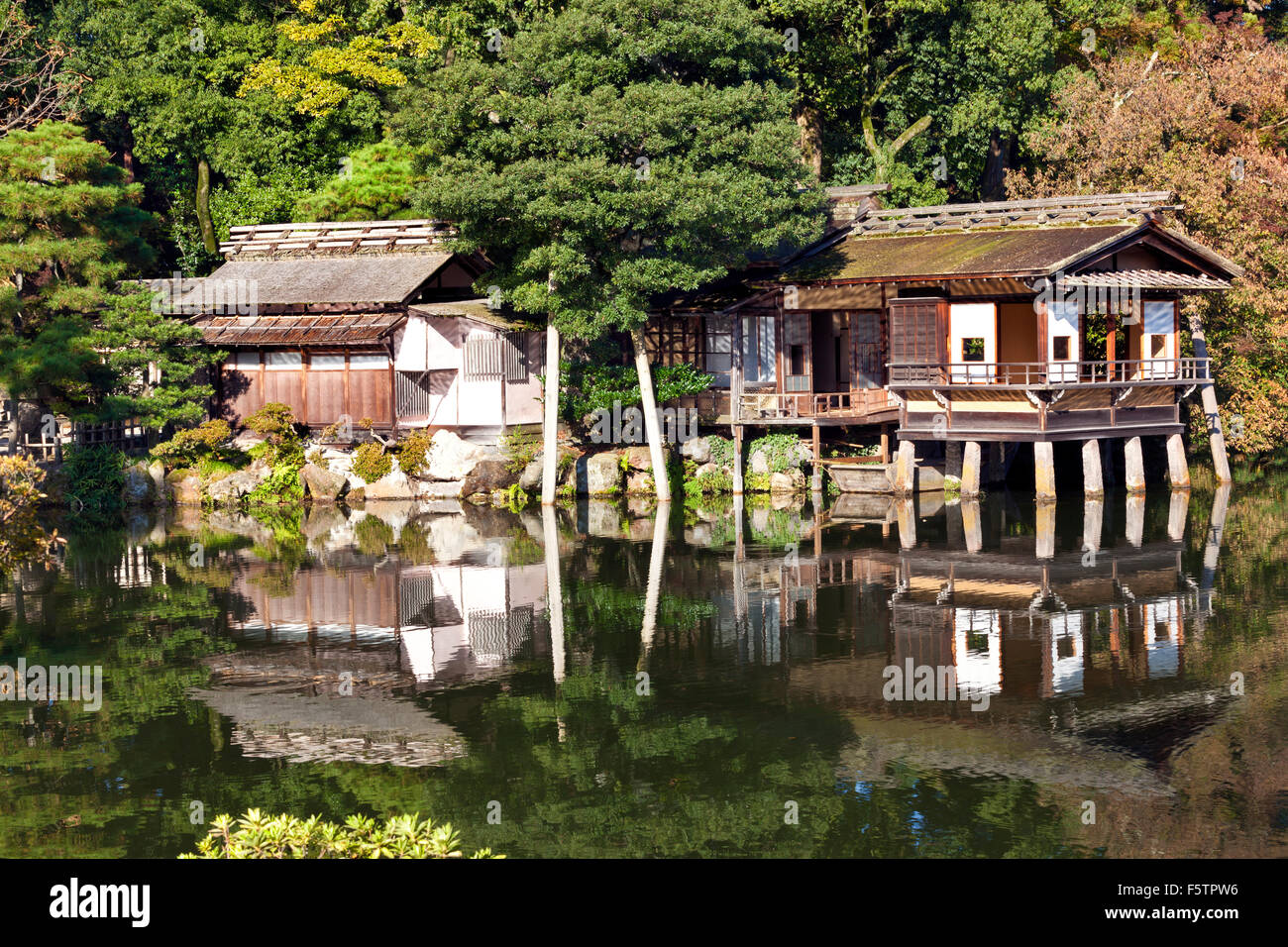 Il vecchio tradizionale teahouse giapponese sul bordo del giardino del lago con riflessi nell'acqua e alberi di pino su un autunno soleggiato da Foto Stock